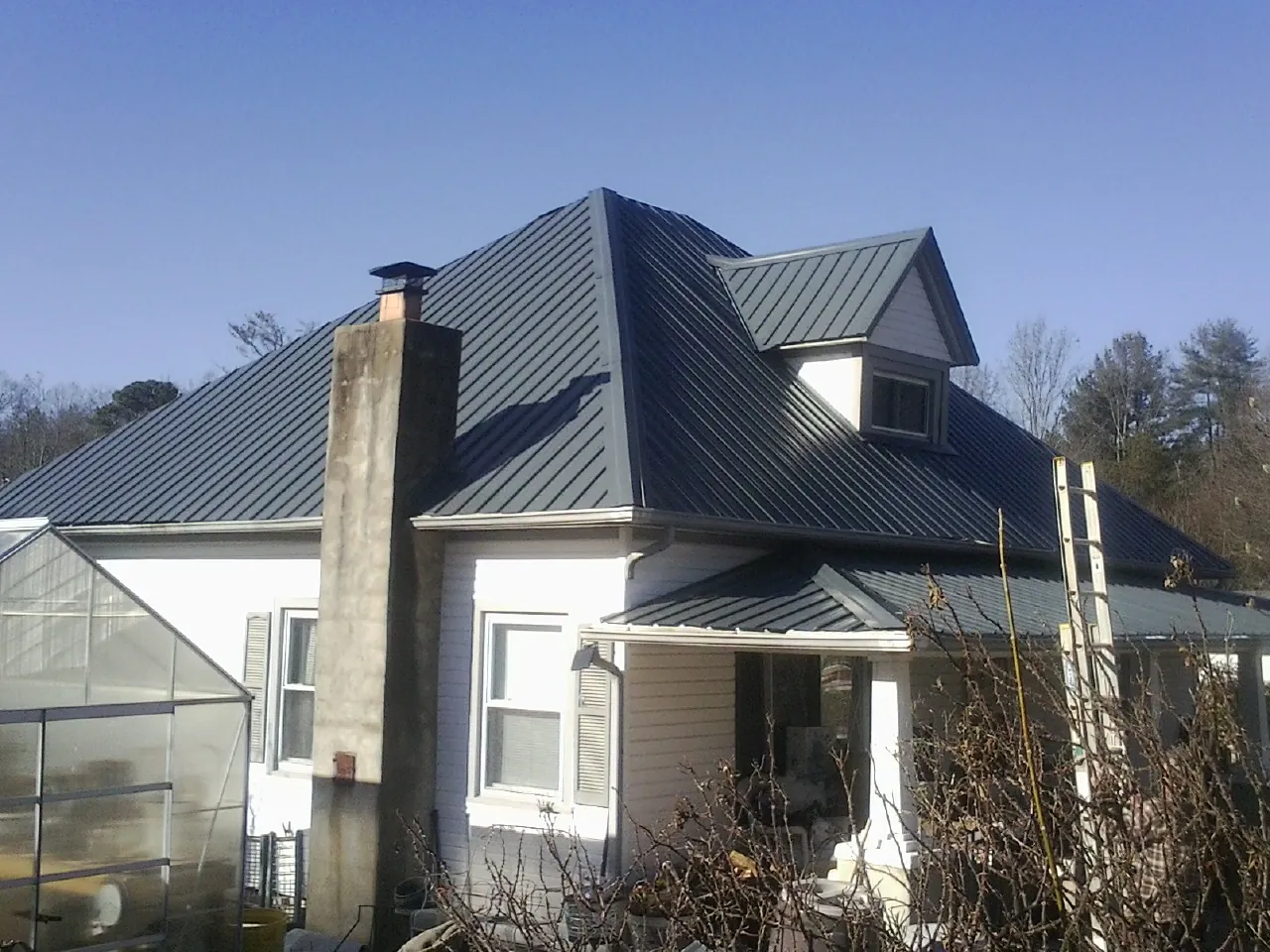 Dark blue standing seam metal roof on a white farmhouse with dormer — Slate & Tile Roof Repair by Roofing Brothers in Newfane