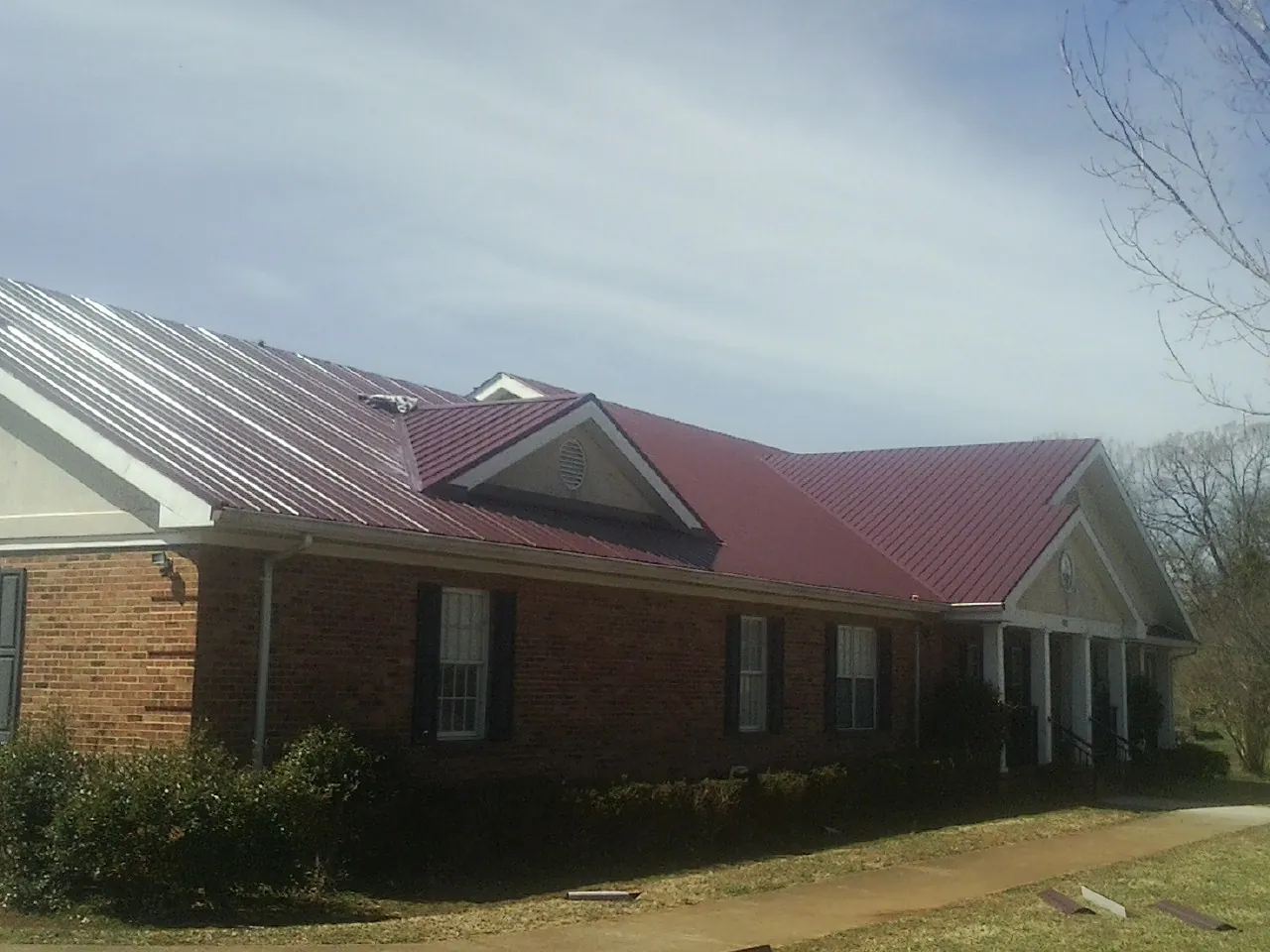 Red metal roof with gabled entries on a long brick building, from a Hail Damage Roof Repair job in Newfane
