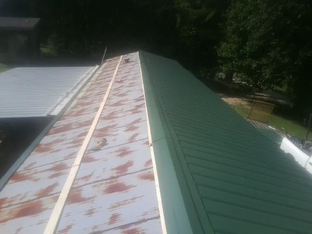 Old rusted panels beside newly installed green metal roofing — Wind Damage Roof Repair by Roofing Brothers in Newfane