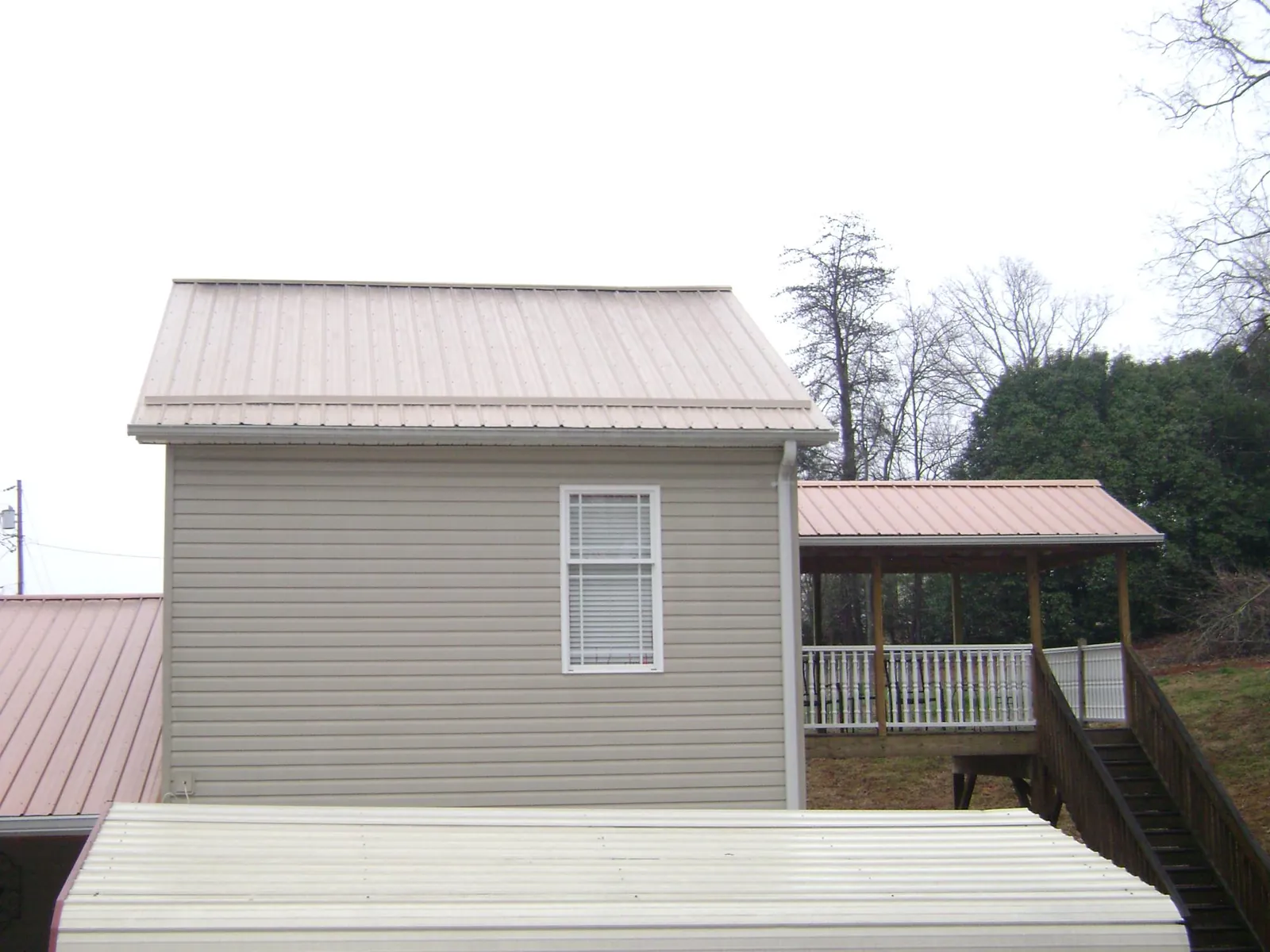 Tan metal roofs on a two story addition and attached porch, from a Roof Replacement job in Newfane